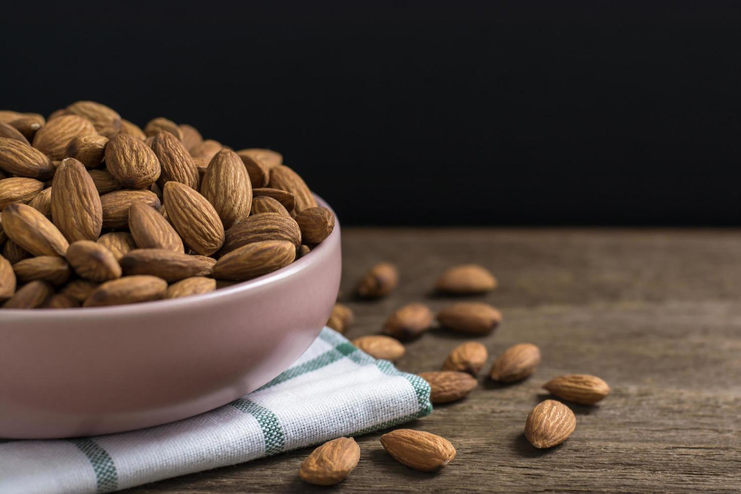 Almonds in pink porcelain bowl on wooden table with copy space photo