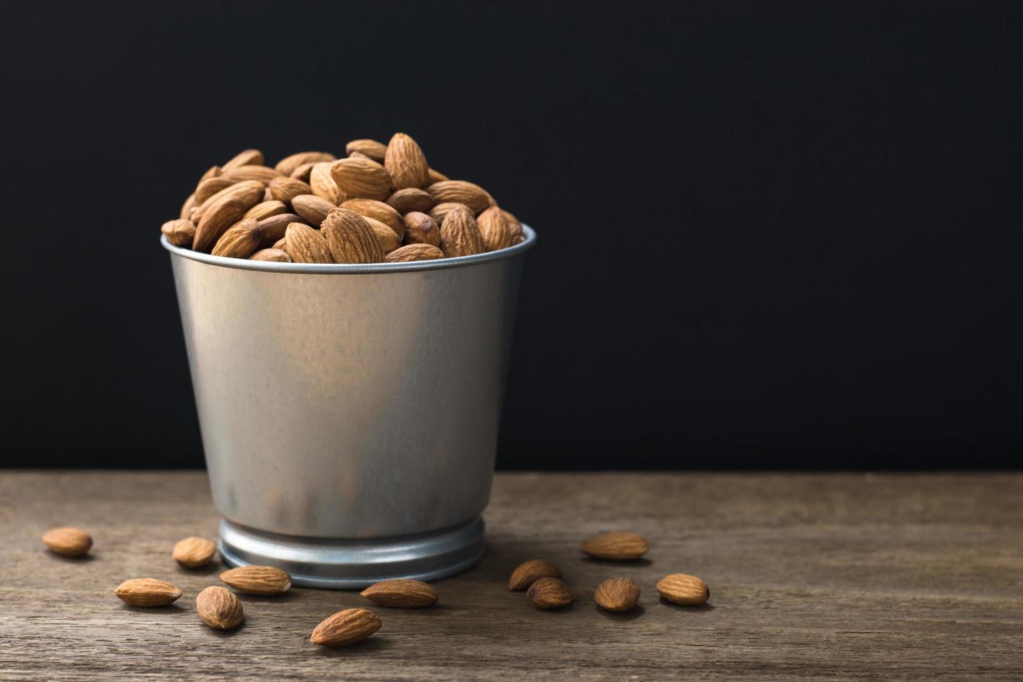Almonds in stainless bucket on wooden table with copy space photo
