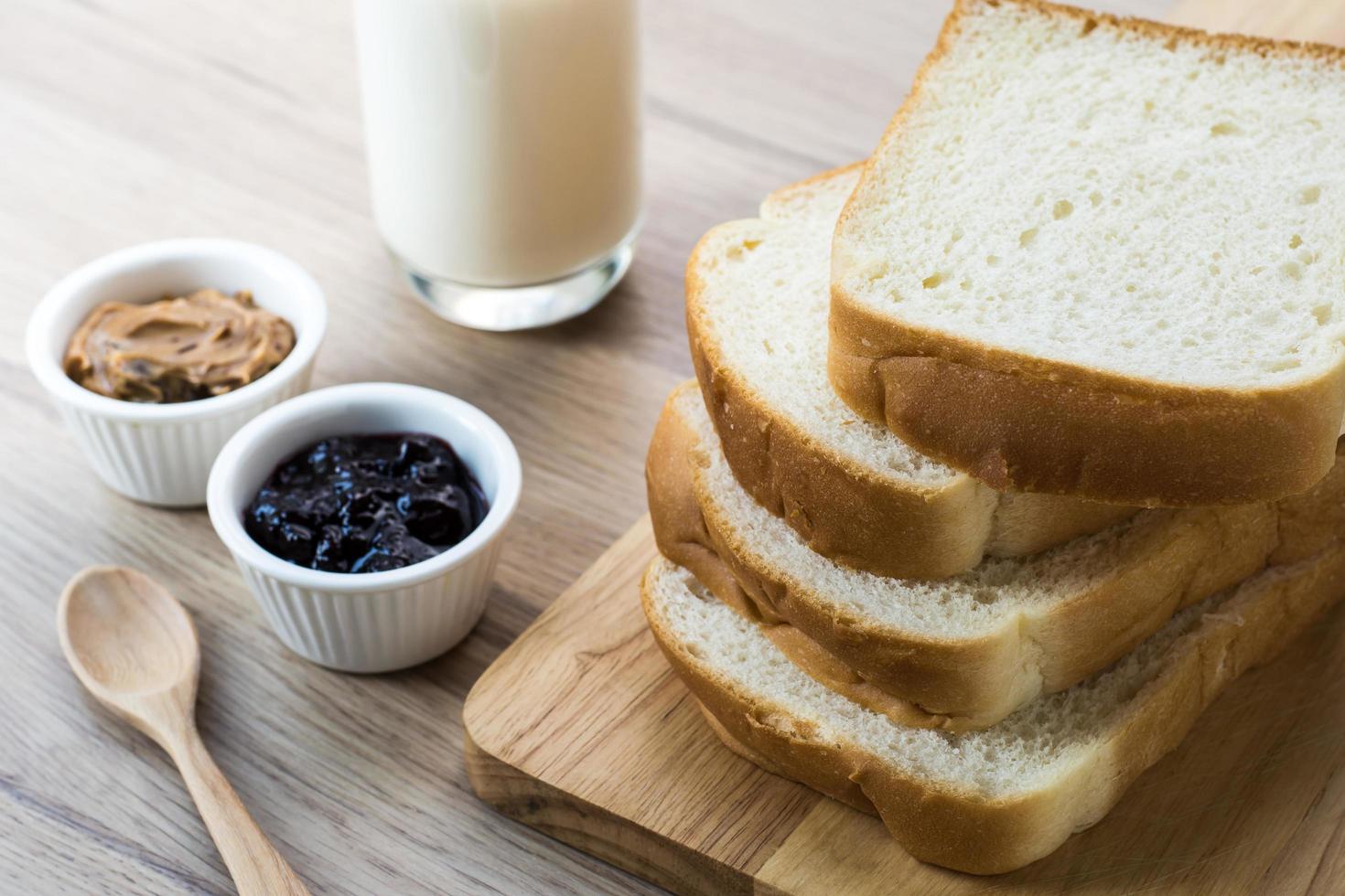 Tabla de madera con rebanadas de pan de desayuno con leche en la mesa de madera y mermelada de grosella negra y mantequilla de maní en la taza pequeña foto
