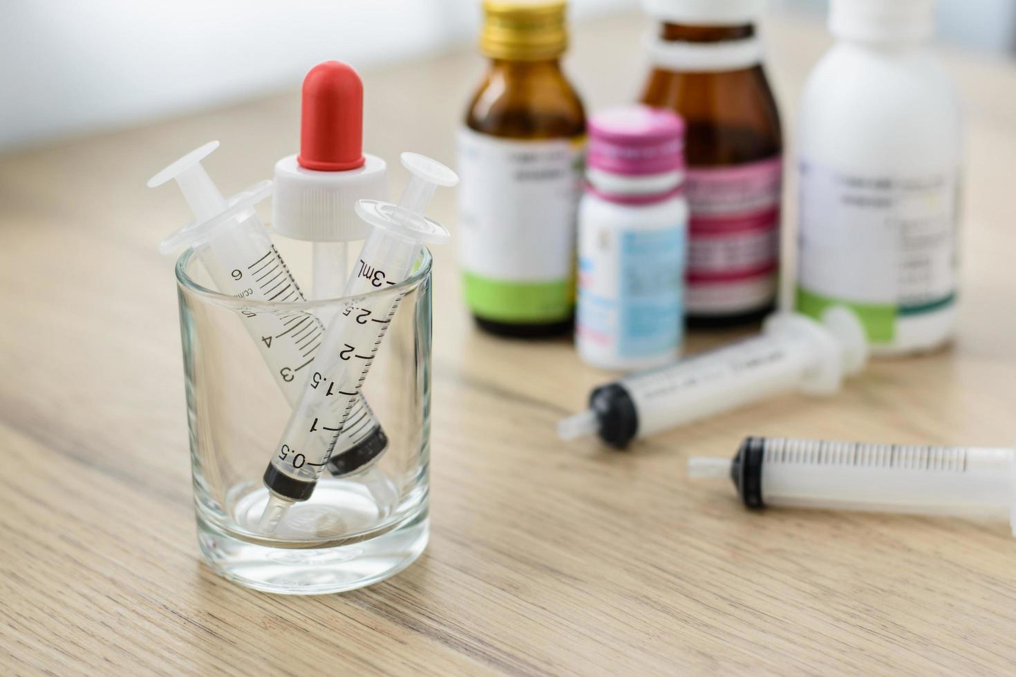 Barril de jeringas vacías en el vaso pequeño sobre la mesa de madera con fondo de botella de medicina blured foto