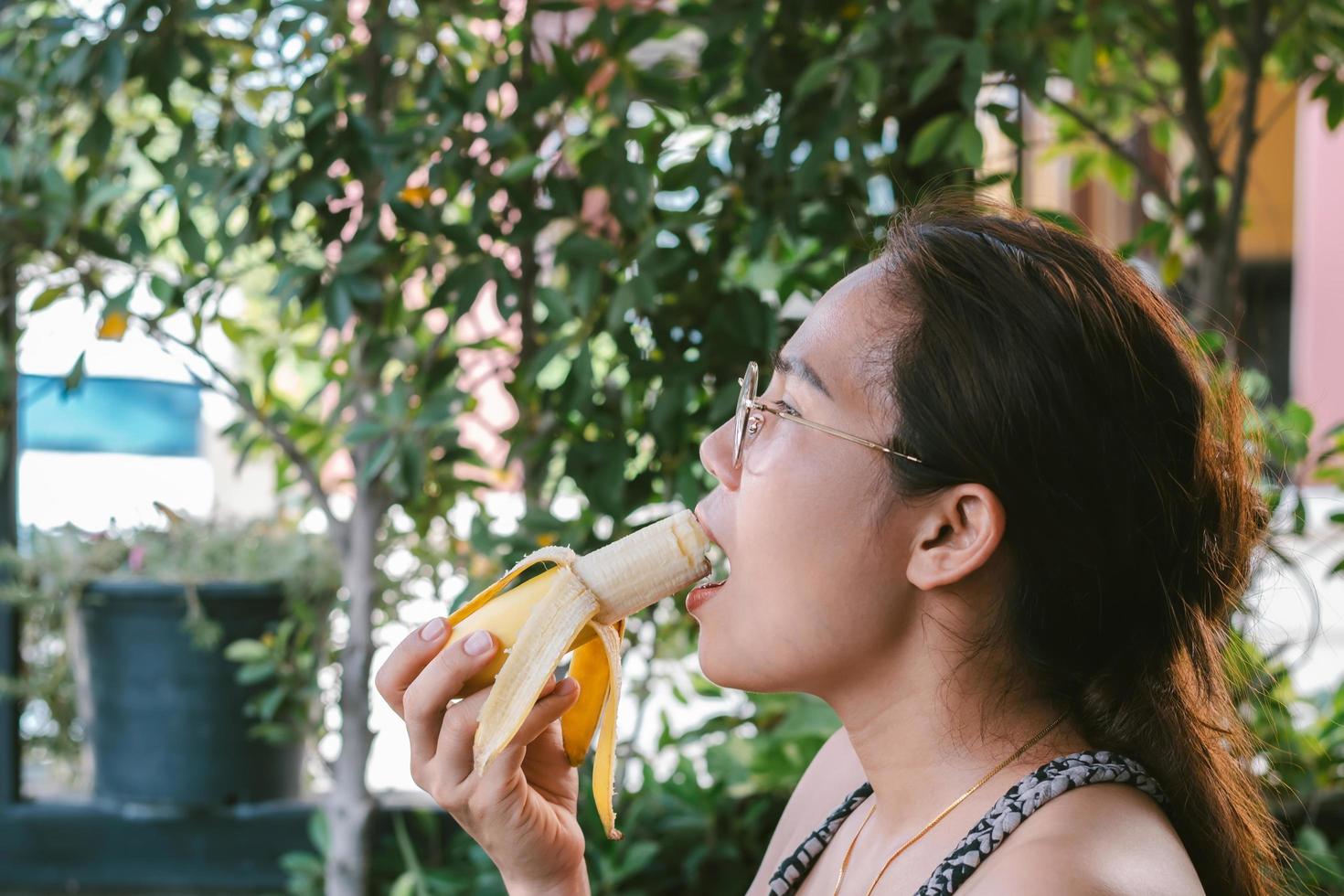 Closeup of a face of an Asian woman in glasses eating a ripe banana photo