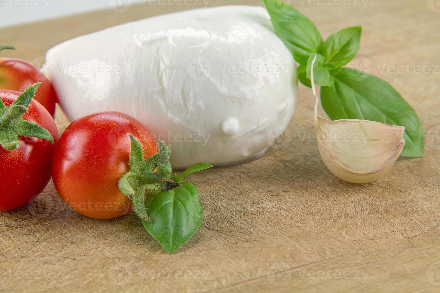 Mozzarella orgánica italiana con tomates cherry y albahaca sobre una tabla para cortar foto