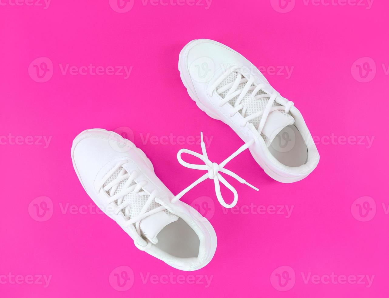 Pair of white sport shoes connected with laces bow on pink background photo