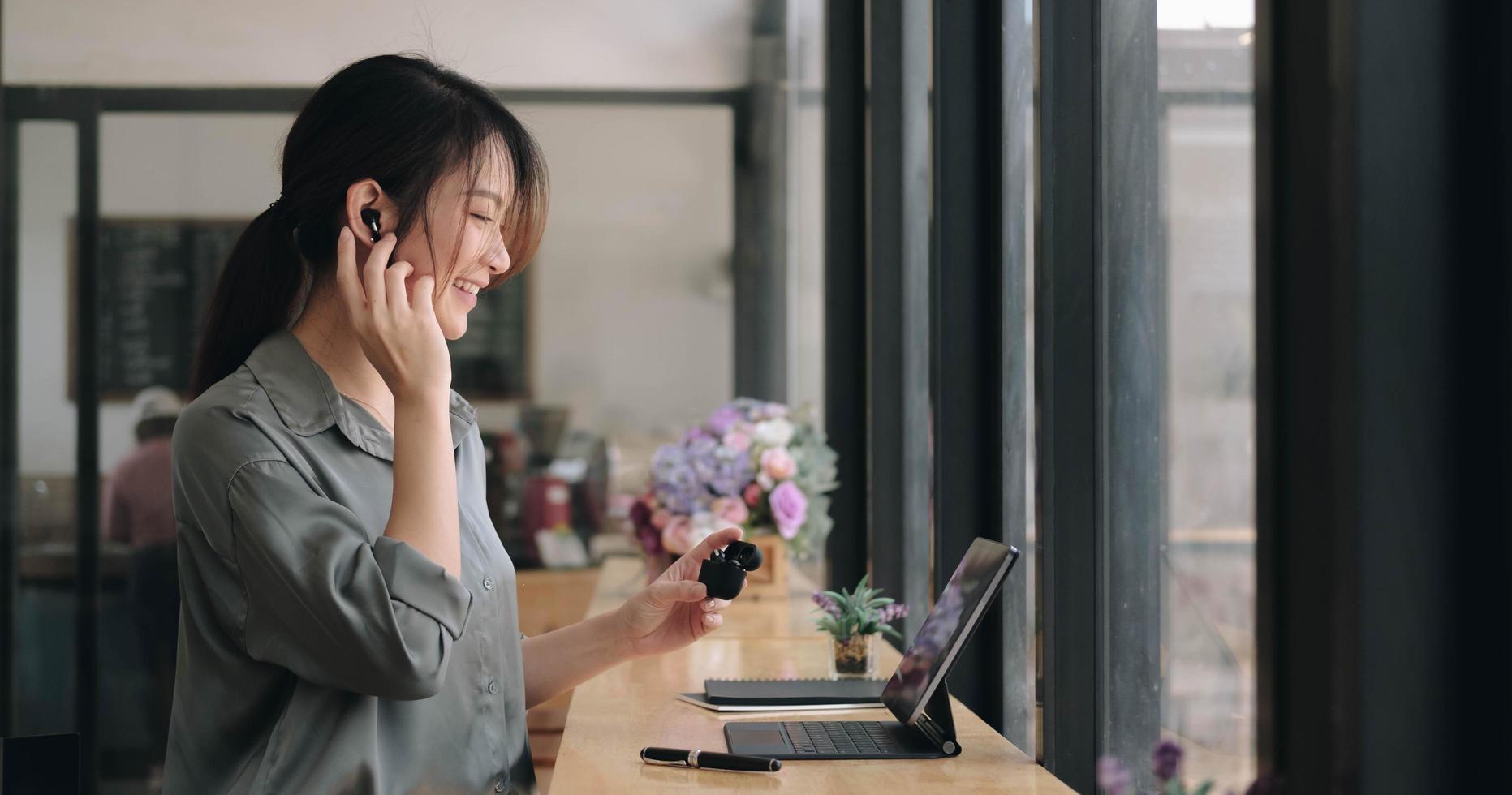 Cerca de joven asiática use auriculares inalámbricos para tener cursos de idiomas en línea y buscar información a través de una computadora portátil en el café foto
