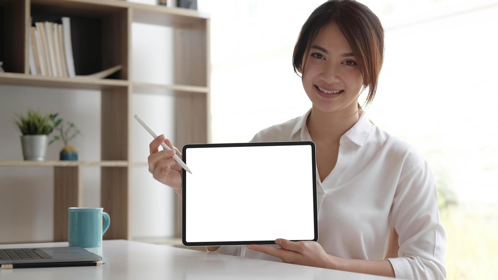 Vista de cerca de la trabajadora mostrando una maqueta de la pantalla de la tableta mientras está de pie en la habitación de la oficina foto