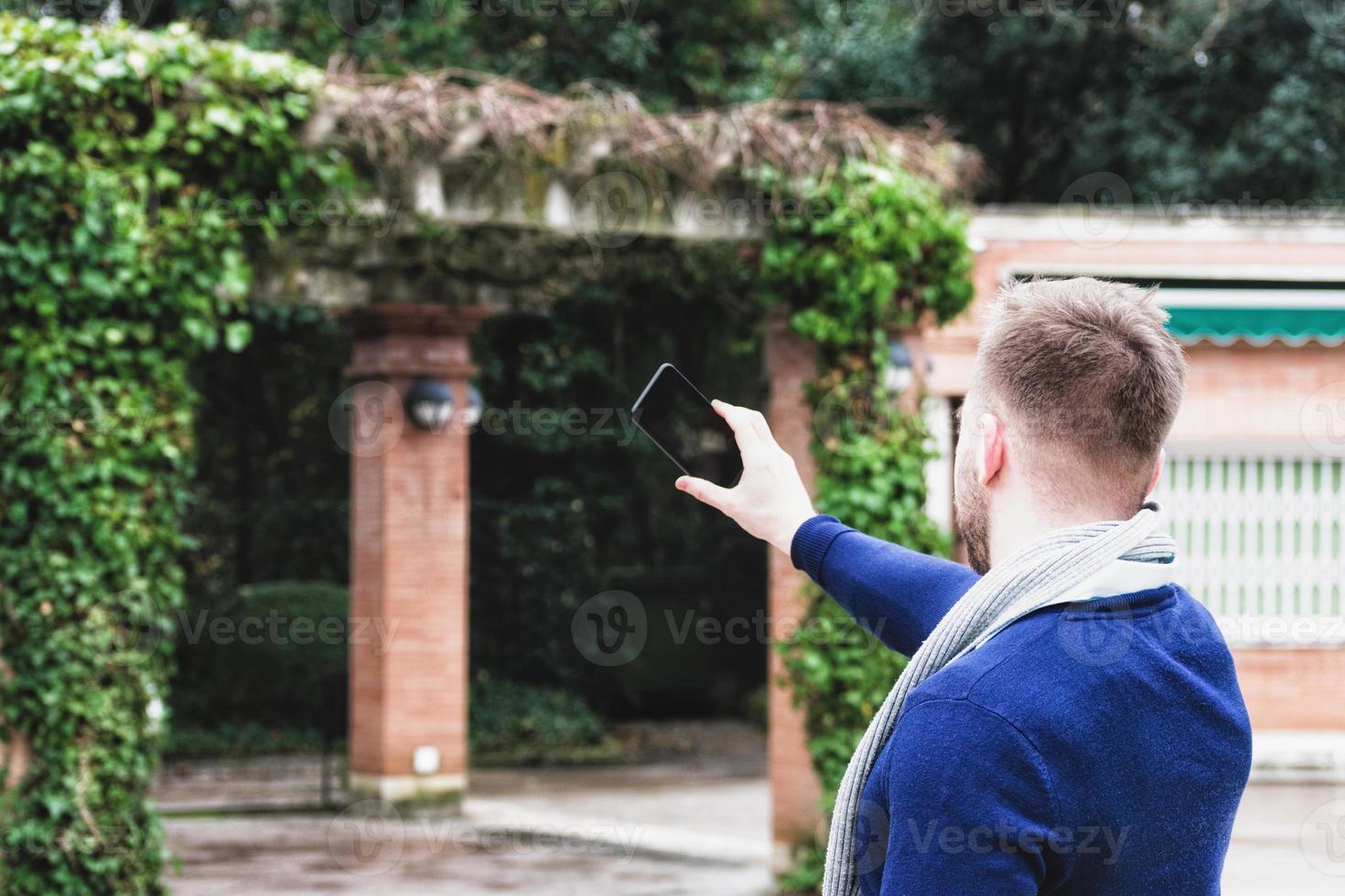 joven de espaldas a la cámara tomando una foto con su teléfono celular