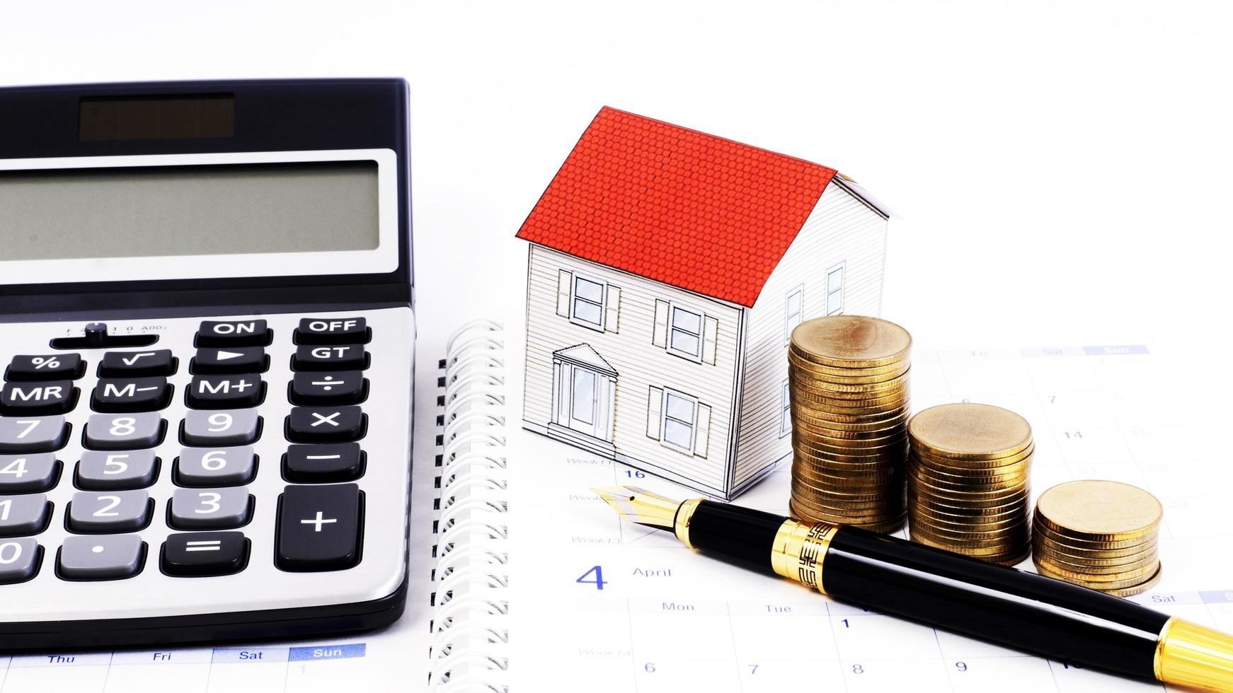 Mortgage loans concept with Fountain pen and money coins stack and paper house and calculator on calendar book pages photo