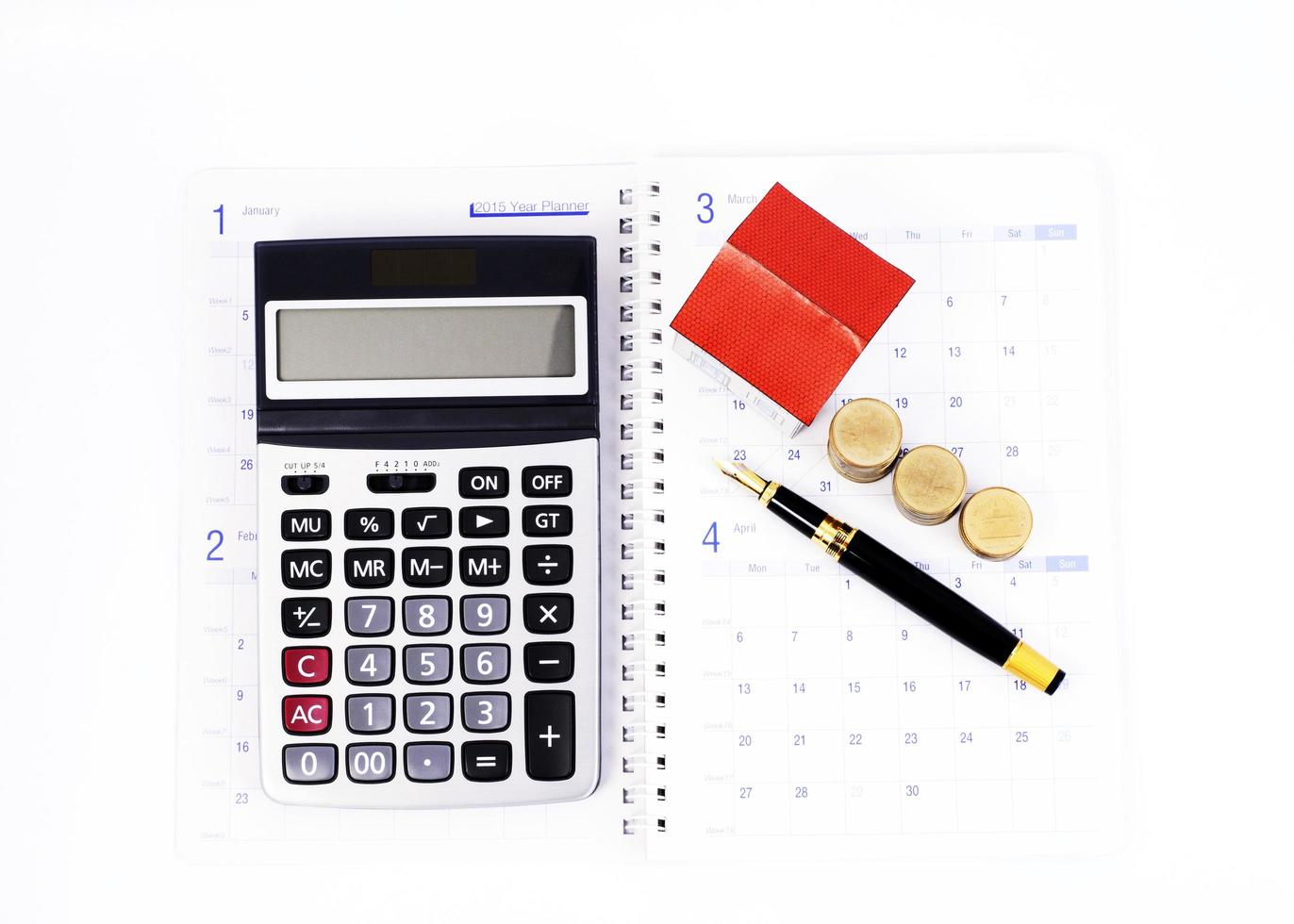 Calculadora y pluma estilográfica y pila de monedas y casa de papel en las páginas del libro de calendario para el concepto de préstamos hipotecarios foto