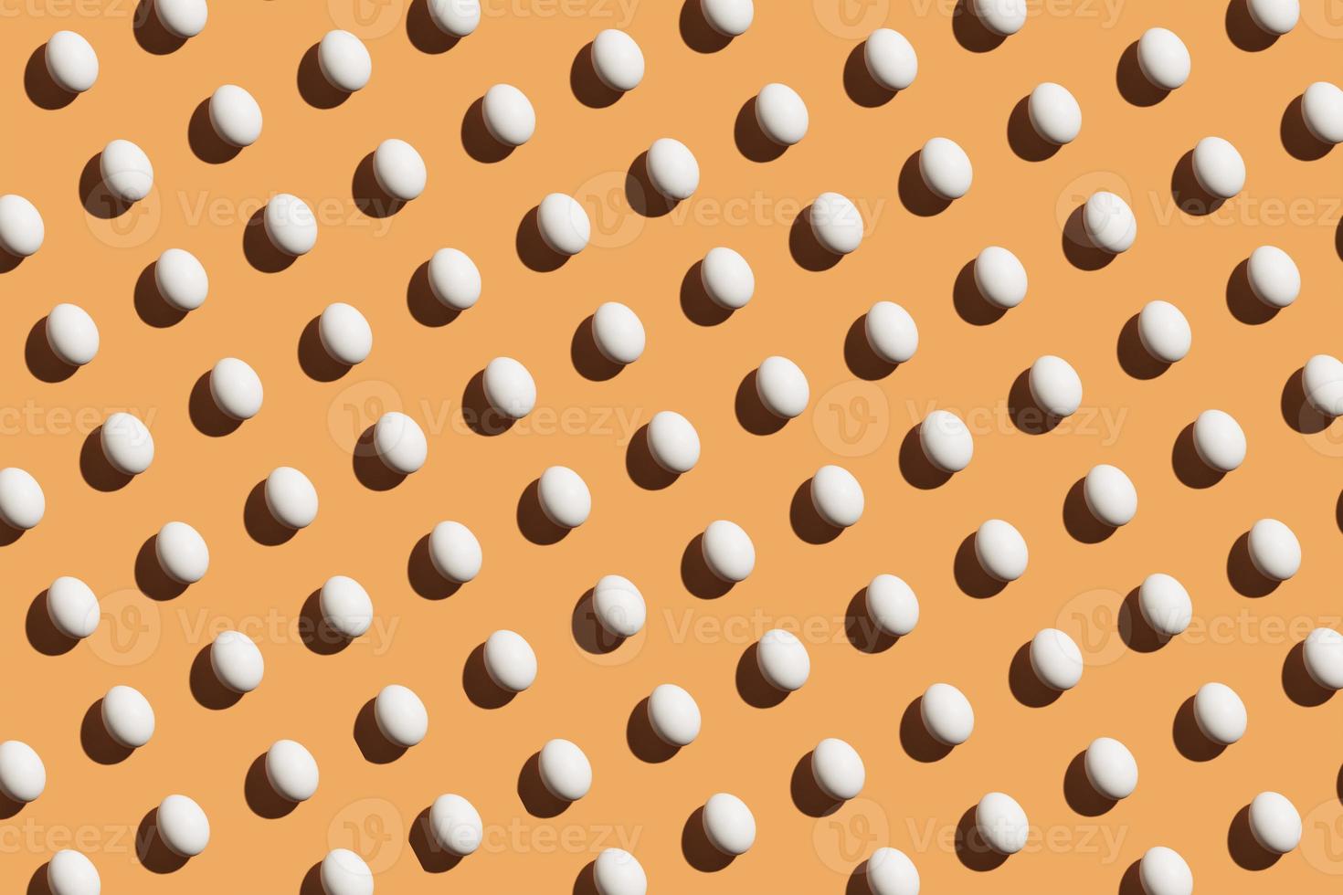 Minimal pattern made of white eggs under bright light with dark shadows on orange background photo