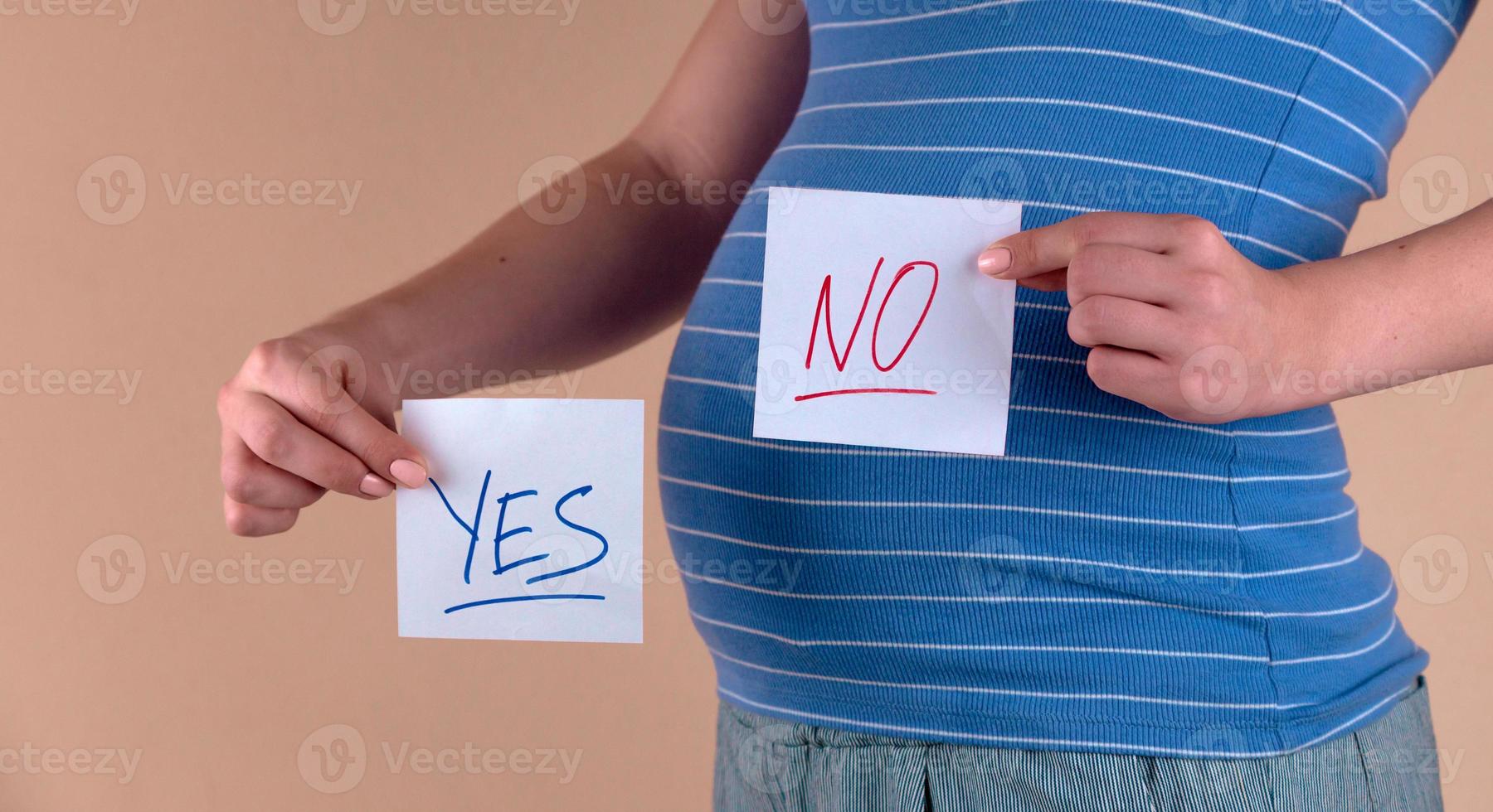 A close up view of the belly of a pregnant woman with the words YES and NO photo