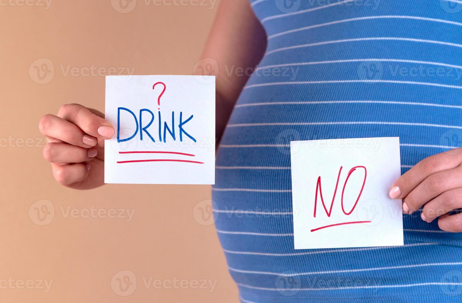 Belly of a pregnant woman in a blue t-shirt with the words Drink and NO photo