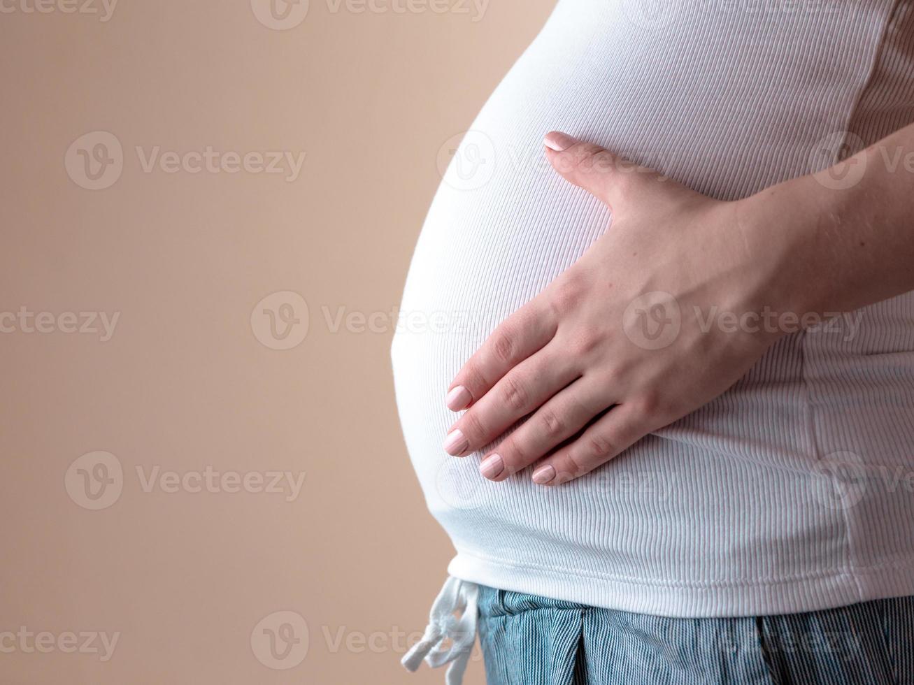 Authentic close-up shot of an young pregnant woman in pajamas caressing her belly photo
