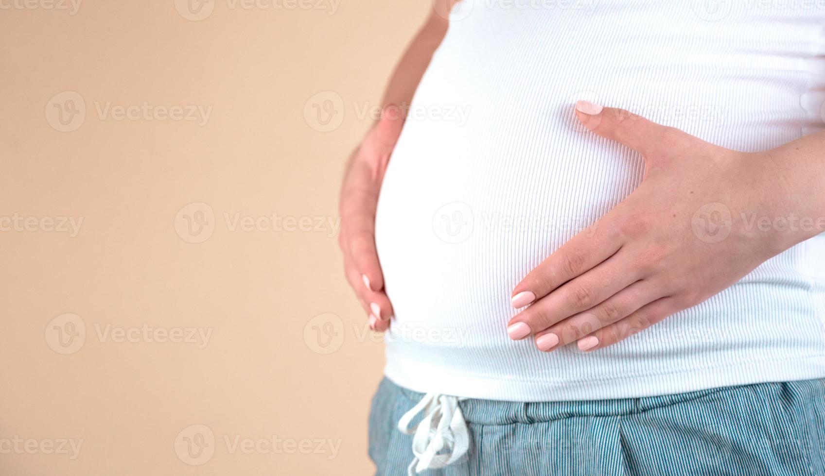 Authentic close-up shot of an young pregnant woman in pajamas caressing her belly photo