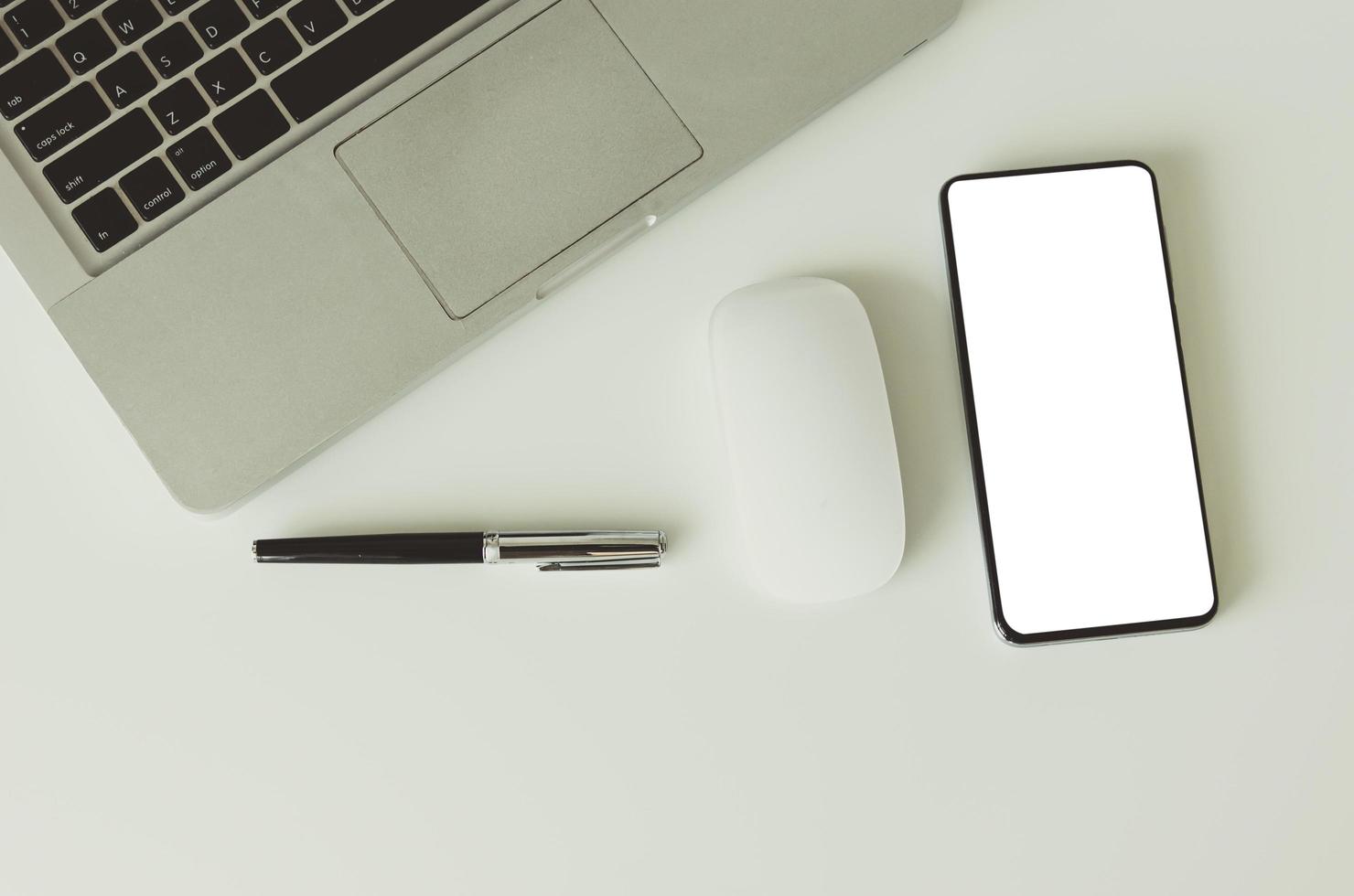 Laptop computer, mouse, pen, and cut out smartphone screen on a white desk photo