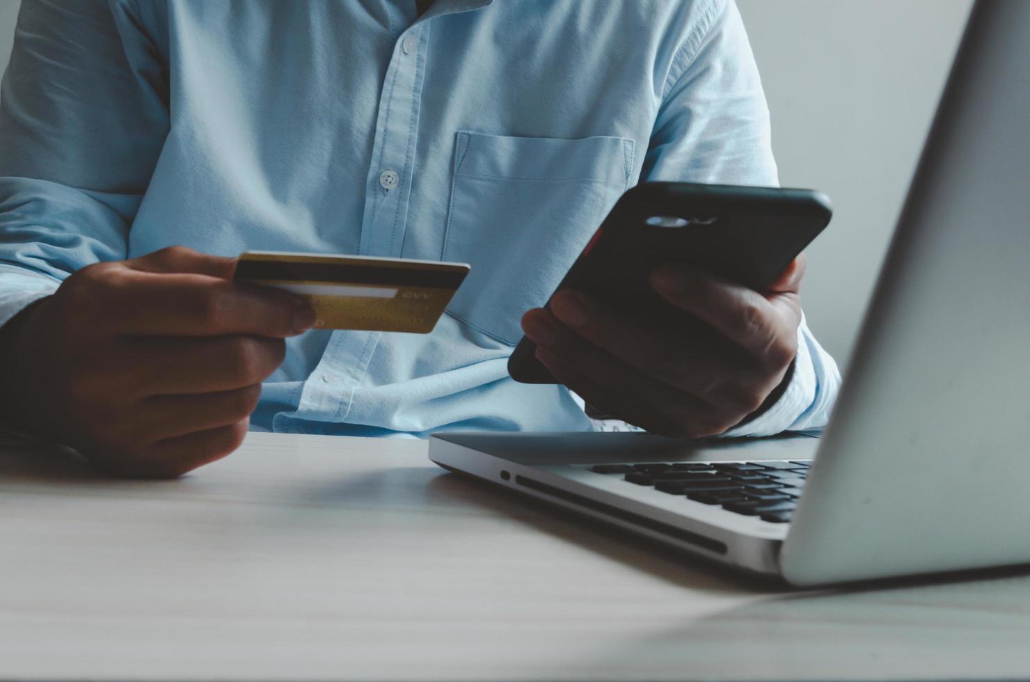 Man holding a smartphone and credit card in front of a laptop computer photo