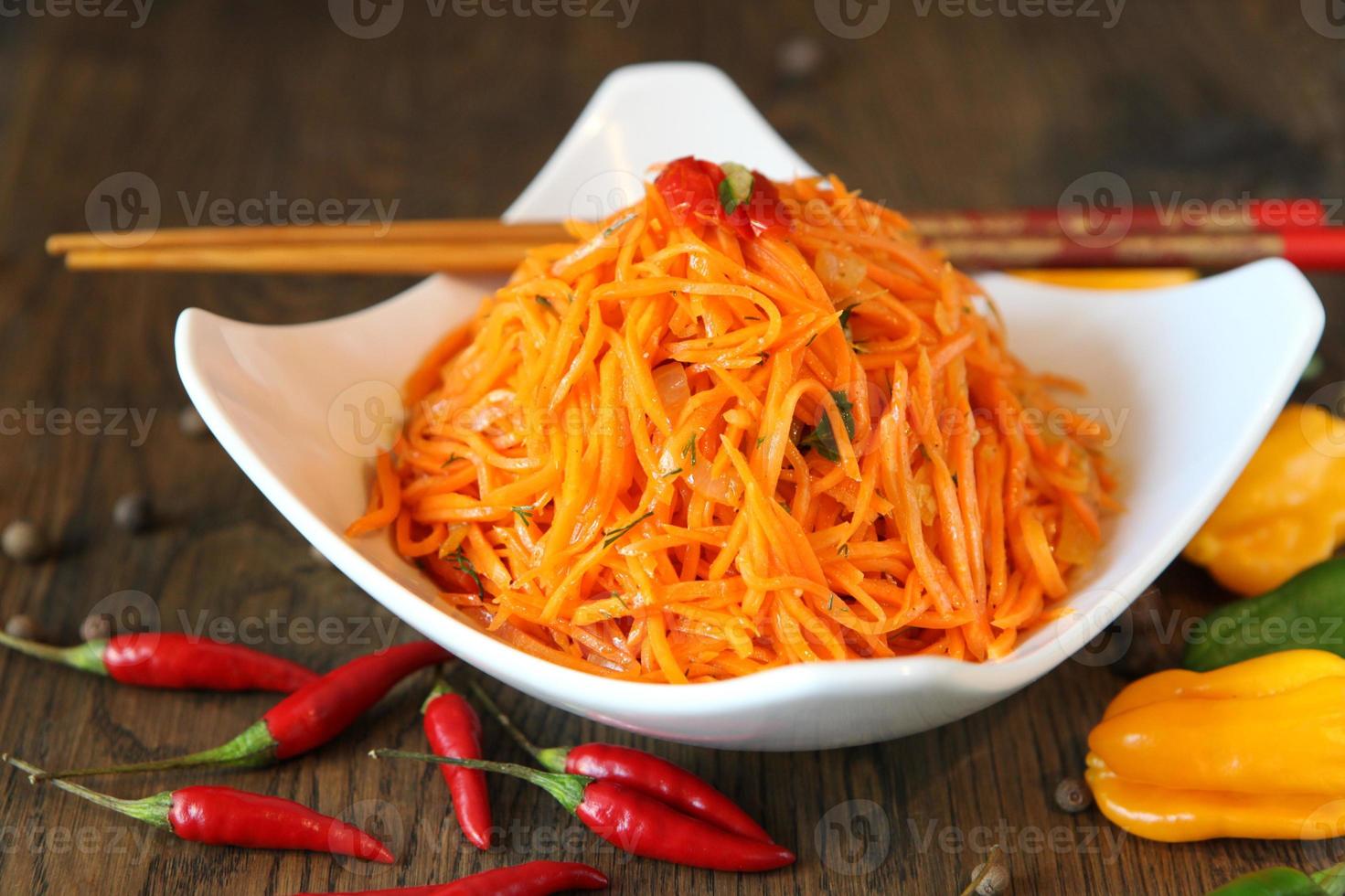 Ensalada de carne coreana de zanahoria con palillos en la mesa de madera de roble foto