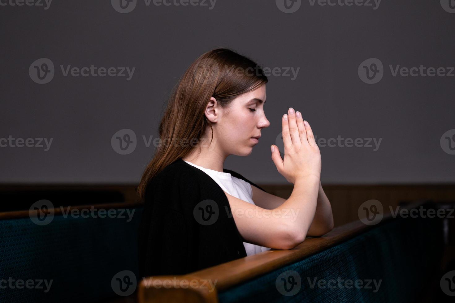 una niña cristiana con camisa blanca está sentada y orando con corazón humilde en la iglesia foto