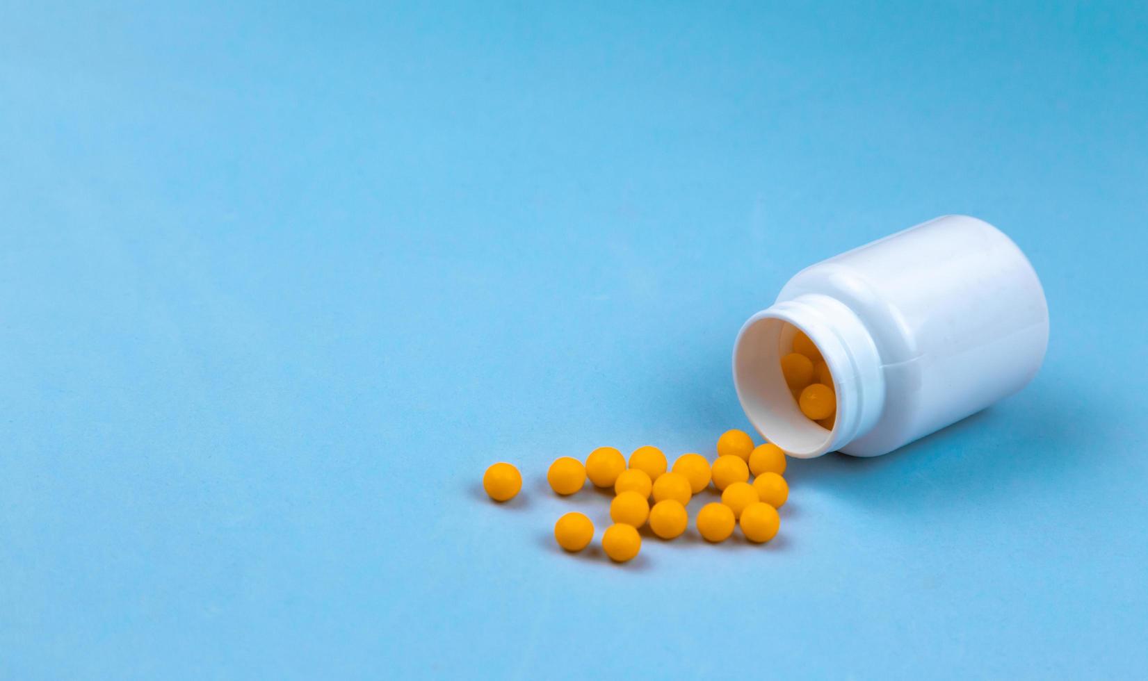 Yellow pills and plastic white bottle on blue background photo