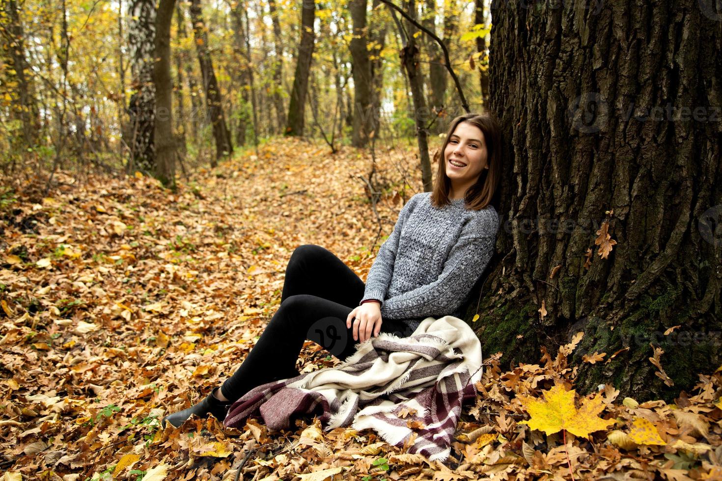 linda chica con una chaqueta gris sentada en el bosque de otoño foto