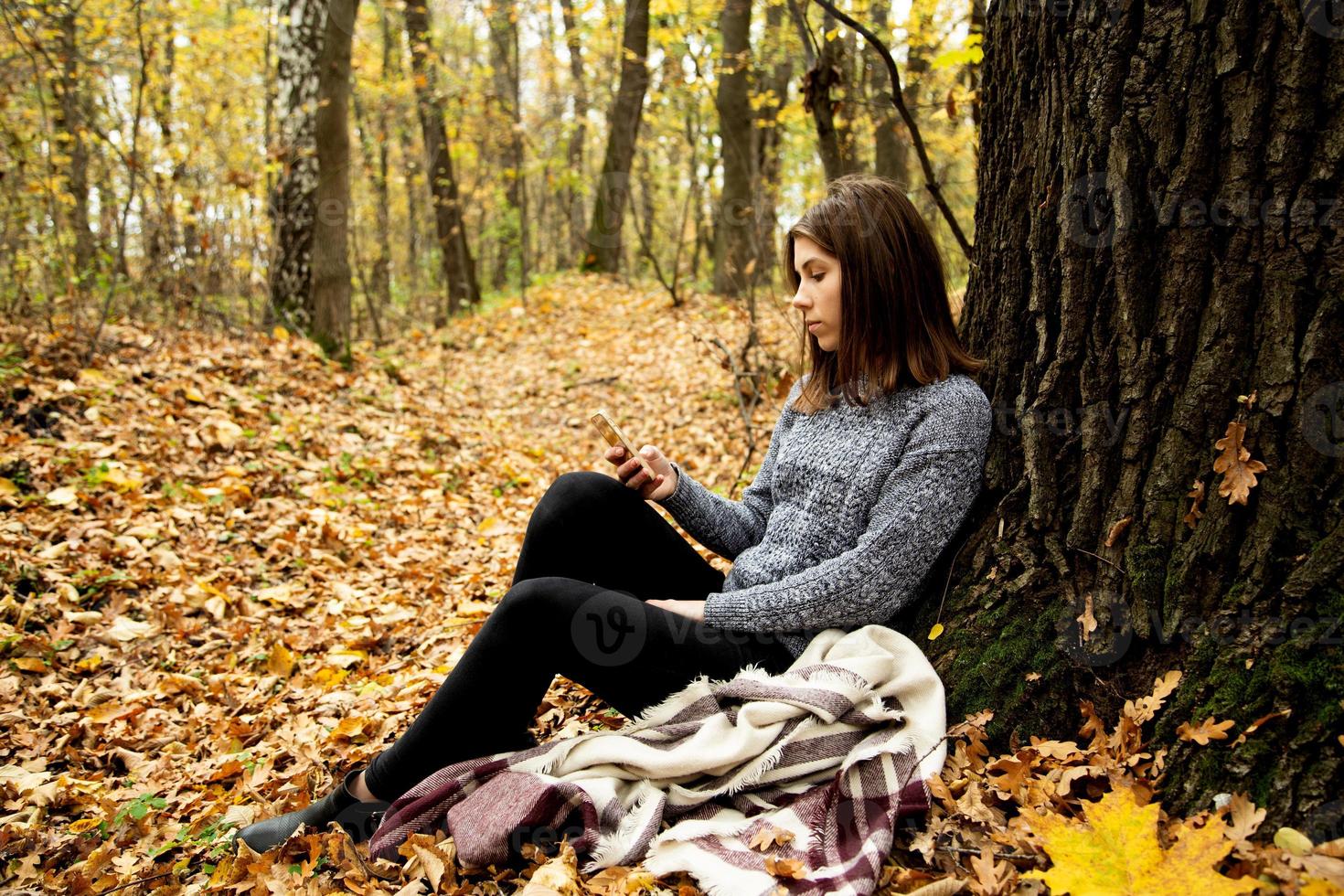 Hermosa joven en una chaqueta gris sentada en el bosque de otoño foto