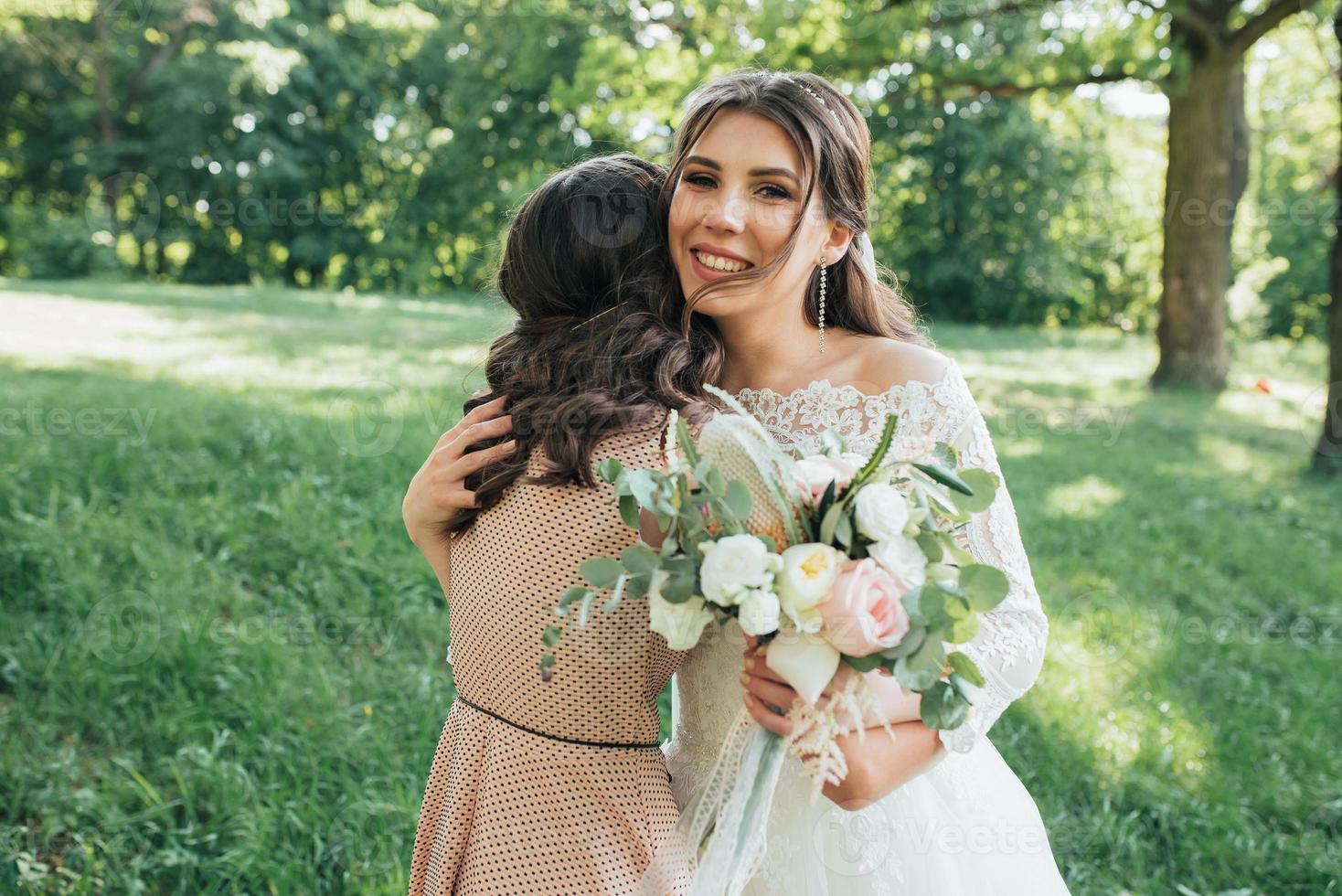 hermosa novia en un vestido de novia en el bosque abrazando a una niña foto