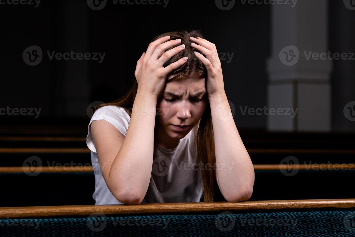una niña cristiana triste con camisa blanca está sentada y orando con corazón humilde en la iglesia foto