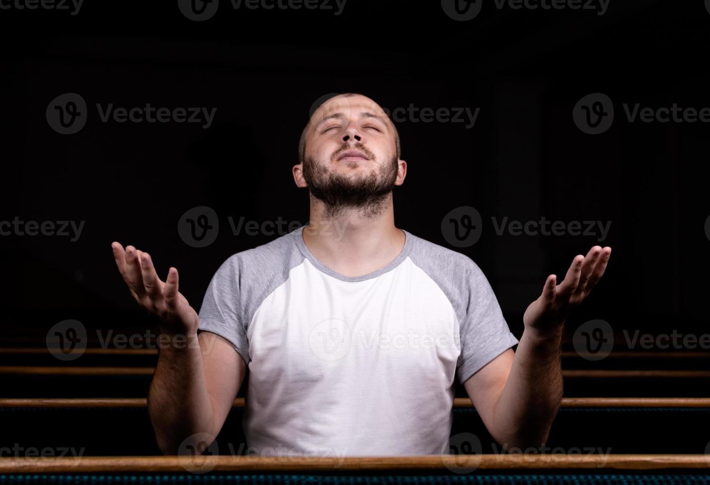 Un hombre cristiano con camisa blanca está sentado con las manos en alto y orando con corazón humilde en la iglesia. foto