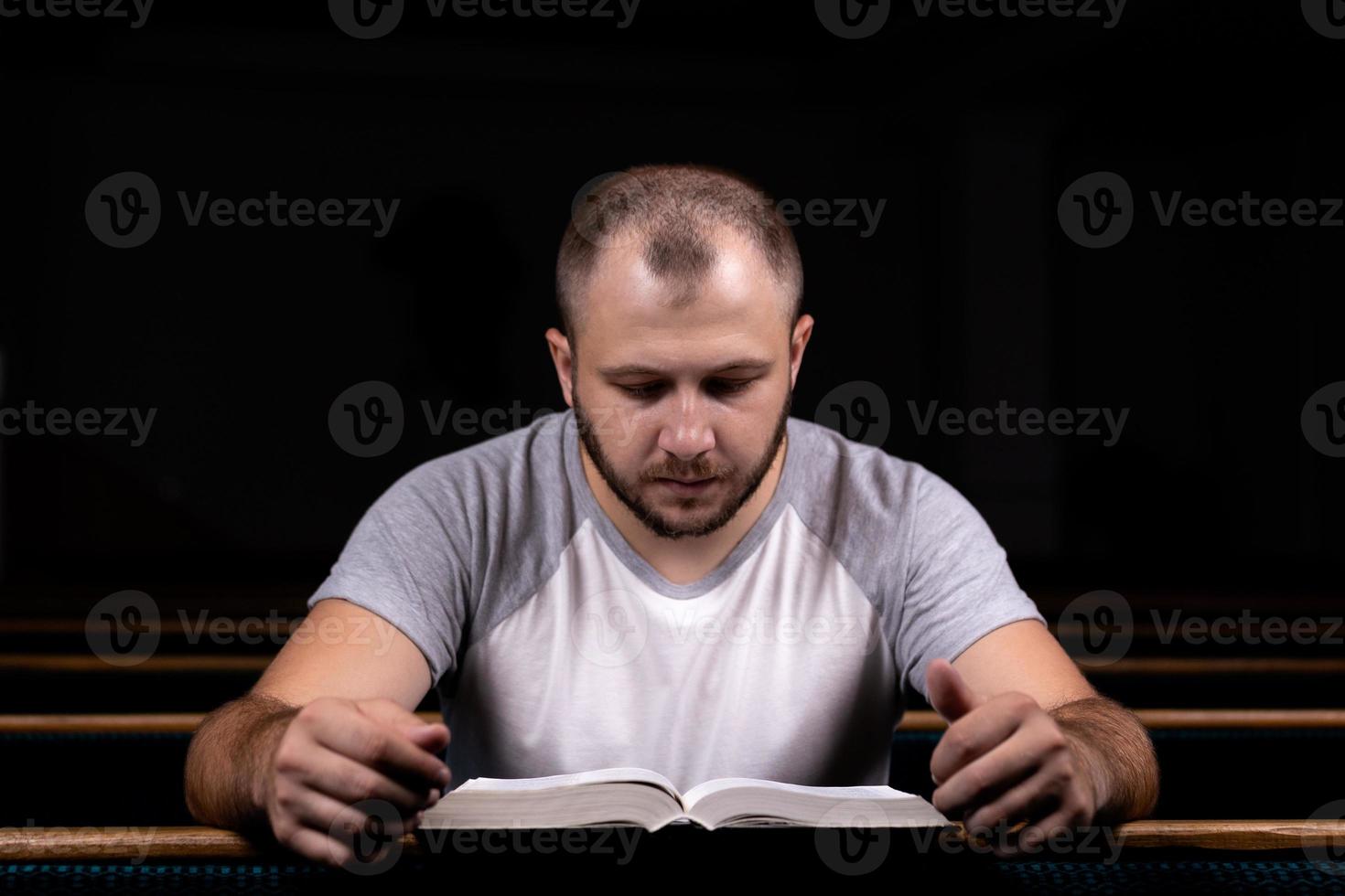 un joven sentado en un banco de la iglesia lee la Biblia y reza foto