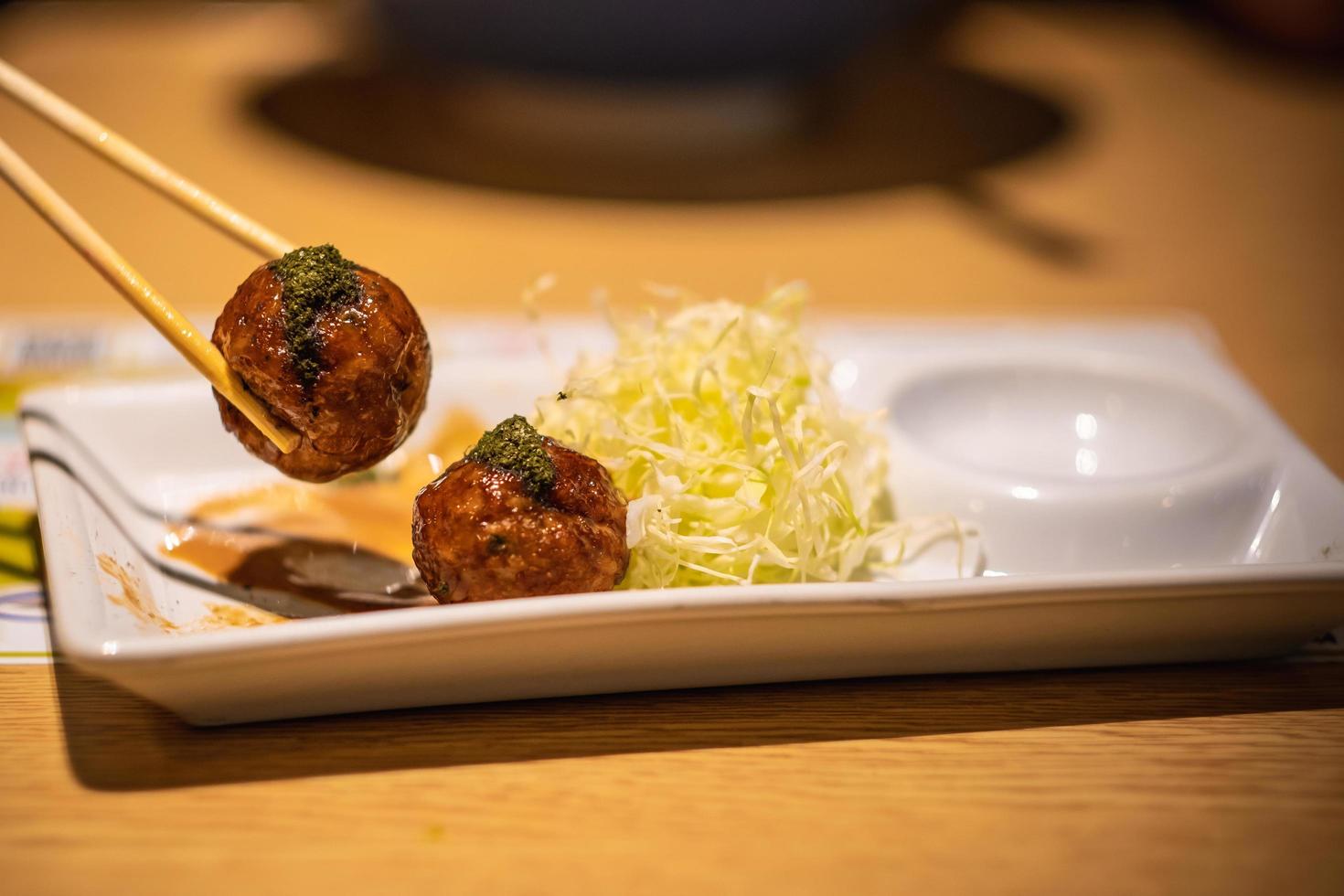 Primer plano de takoyaki, palillo sujetado en bola takoyaki sobre fondo de mesa de madera foto