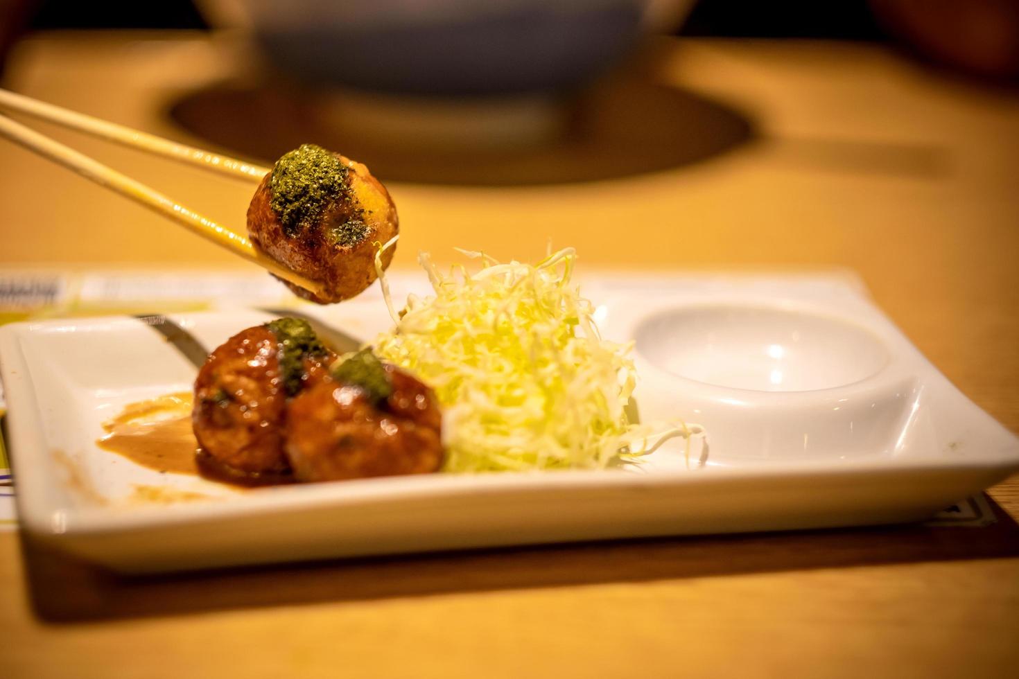 Primer plano de takoyaki, palillo sujetado en bola takoyaki sobre fondo de mesa de madera foto