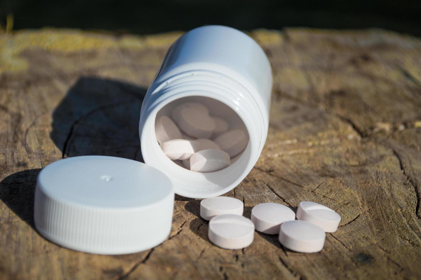 White jar and white pills lie on a stump photo