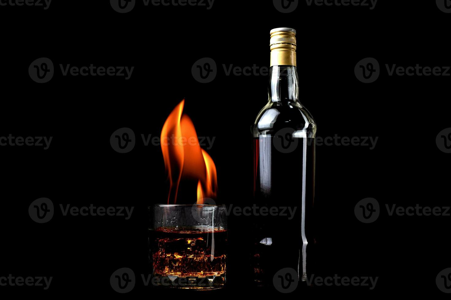 Liquor bottles and whiskey glass with fire flames on black background photo