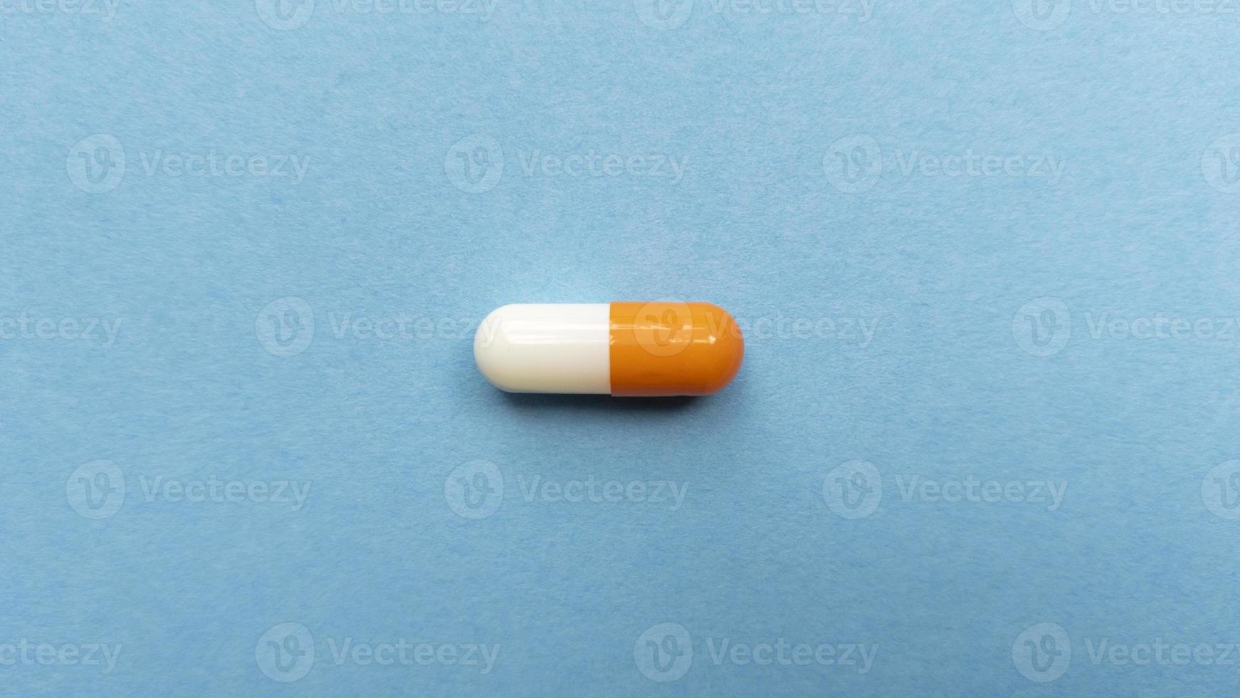 Orange and white single pill capsule on blue background Simple flat lay with pastel texture Medical concept Stock photo