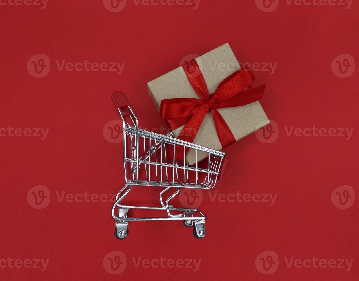 Supermarket trolley and gift box on a red background Shopping concept photo