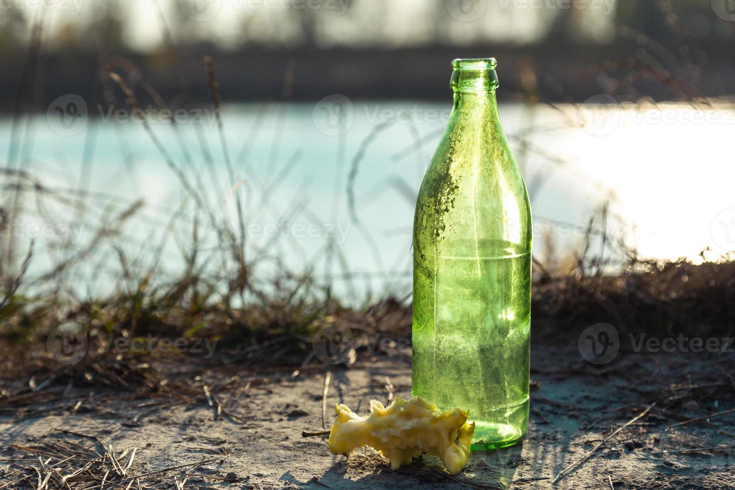 Botella de vidrio sucia en el bosque junto a un trozo de manzana foto