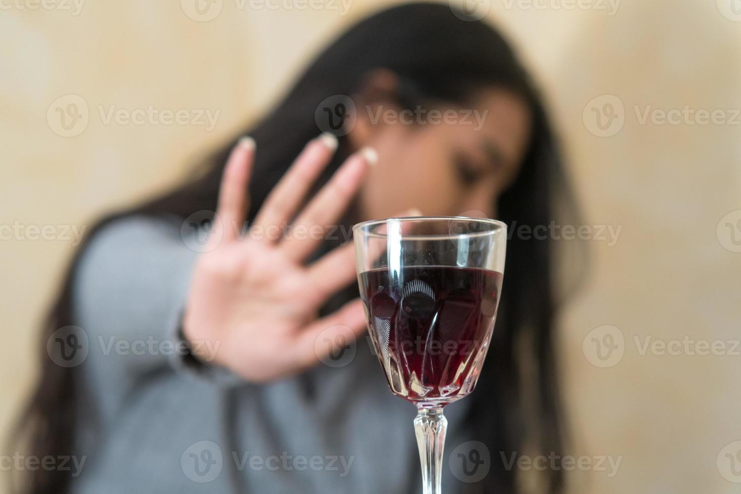 Renunciar al alcohol una mujer joven en la mesa rechaza una copa de vino tinto con la mano foto