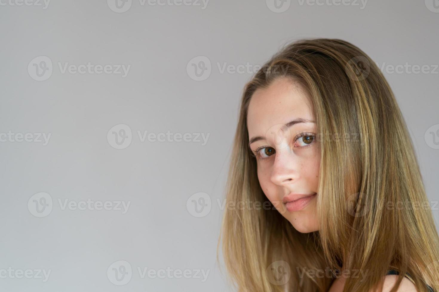 Close up studio portrait of a young back turned woman turning her head looking at the camera over grey background photo