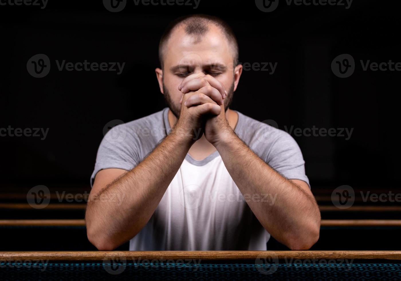 A Christian man in white shirt is sitting and praying with humble heart in the church photo