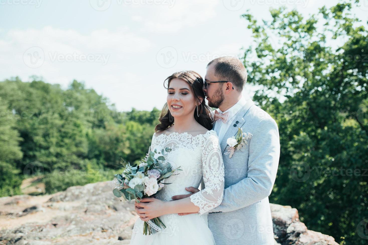 Foto de boda de la novia y el novio en un color rosa grisáceo en la naturaleza en el bosque y las rocas
