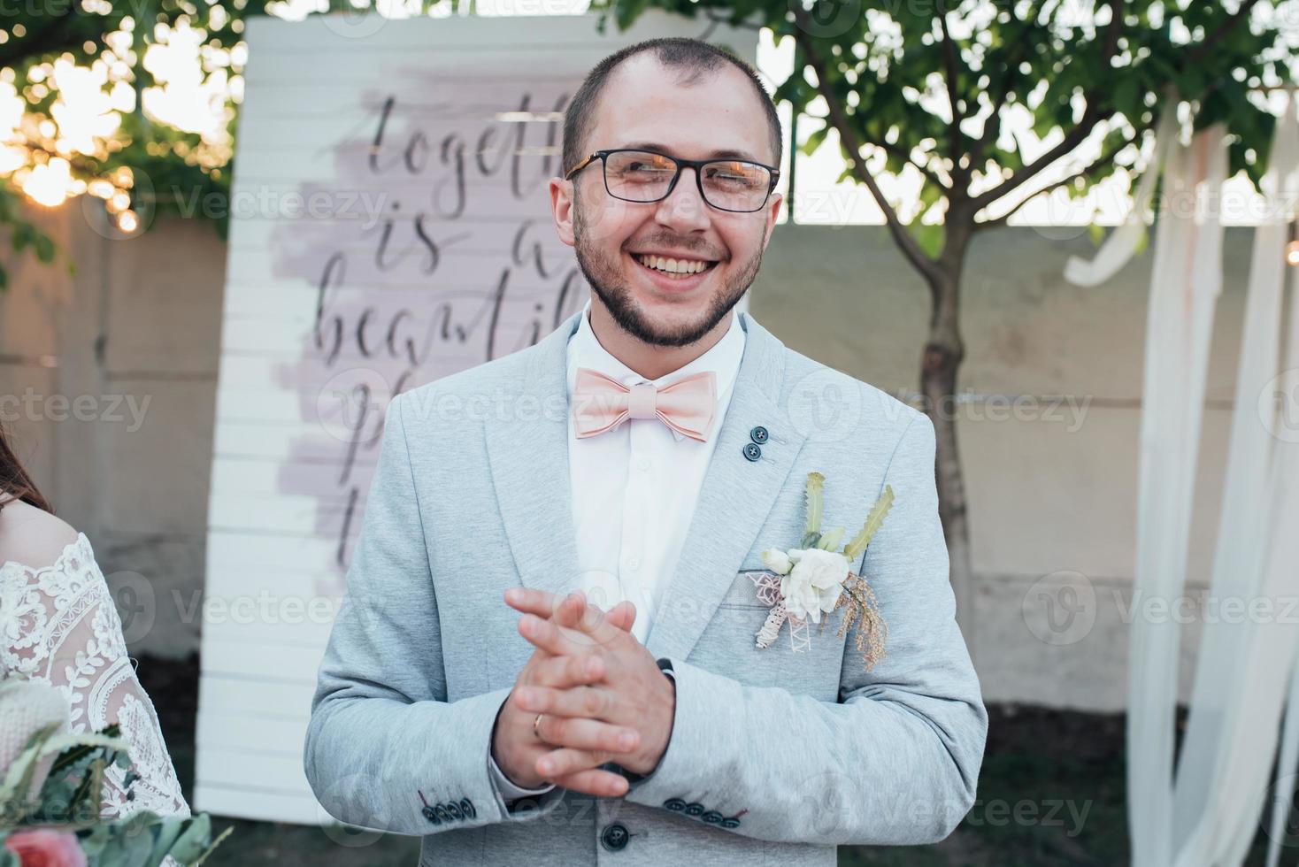 Wedding photo of emotions of a bearded groom with glasses in a gray jacket and rustic style