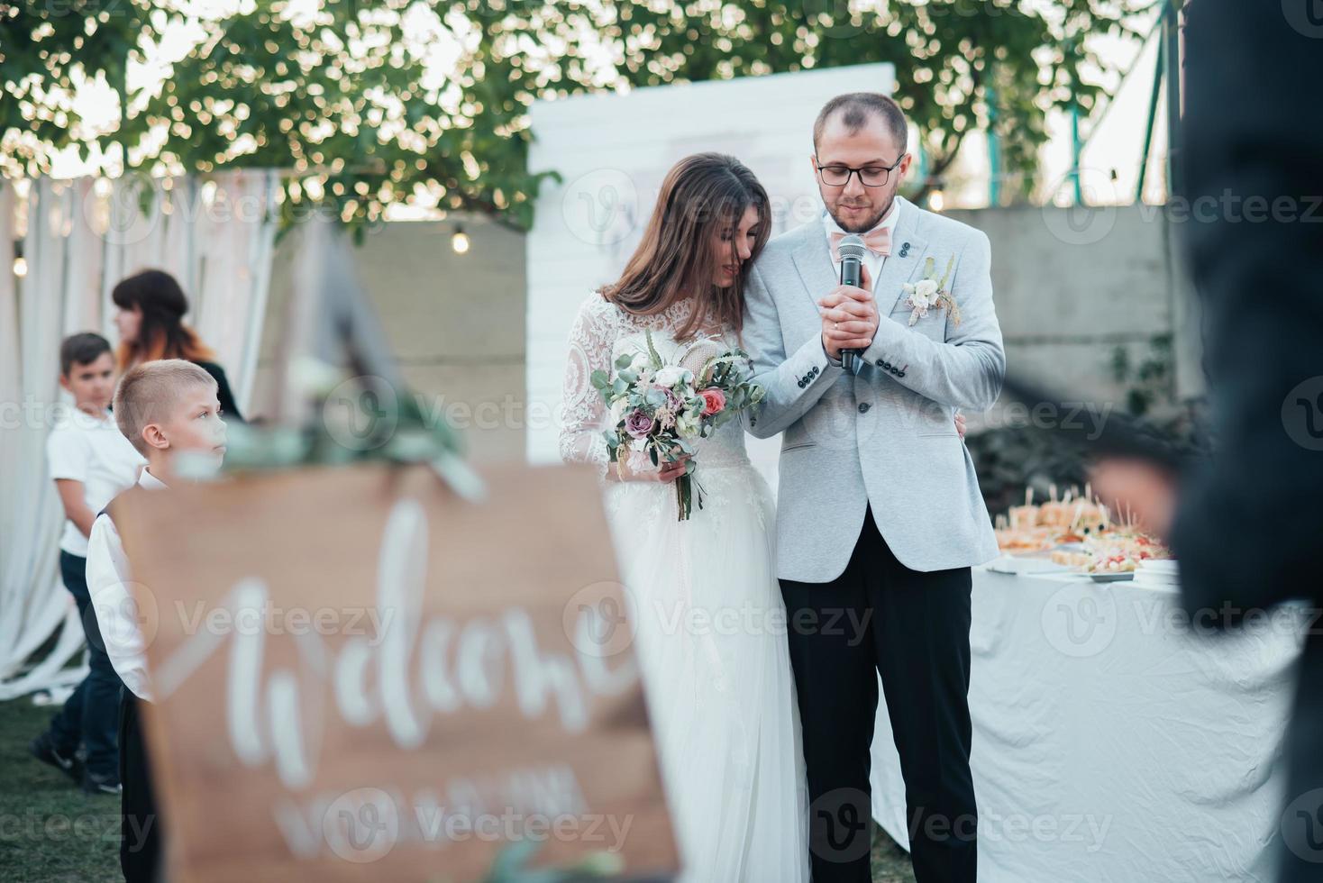 Bride and groom at a wedding party and a wooden easel in the foreground with space for text photo