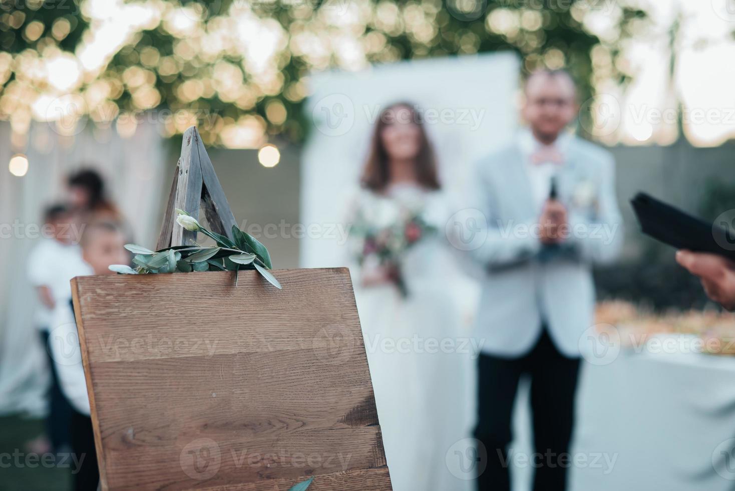 Bride and groom at a wedding party and a wooden easel in the foreground with space for text photo