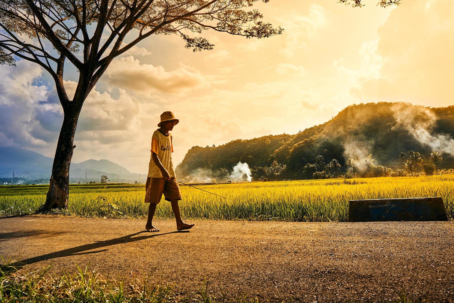 Un anciano caminando sosteniendo una caña de pescar al atardecer. foto