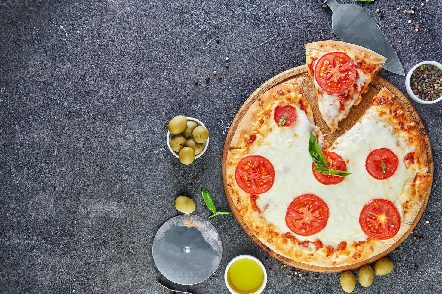 Pizza italiana e ingredientes para cocinar sobre un fondo de hormigón negro tomates aceitunas albahaca y especias foto