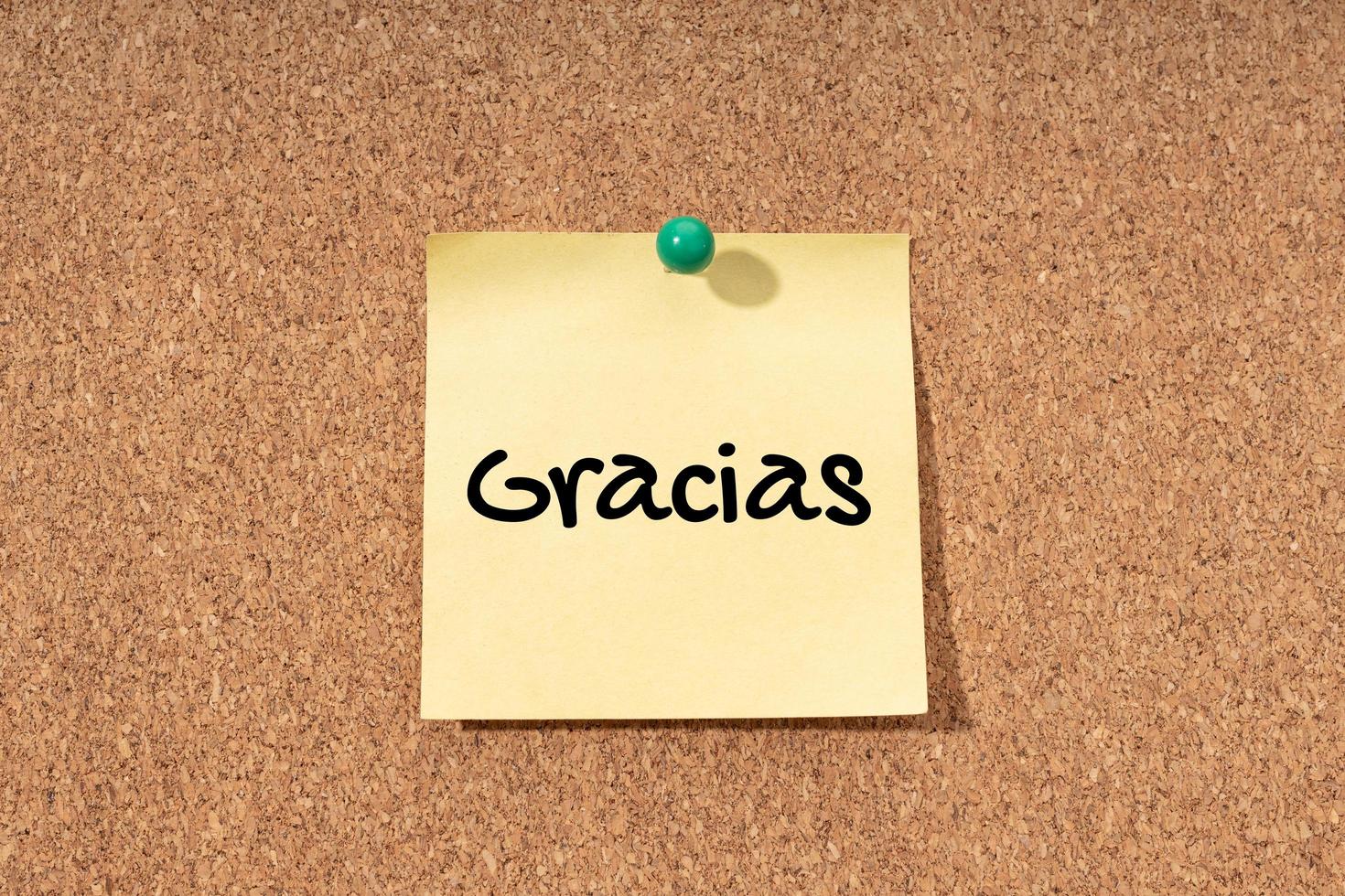 Gracias - palabra de agradecimiento en idioma español en nota amarilla en tablero de corcho foto