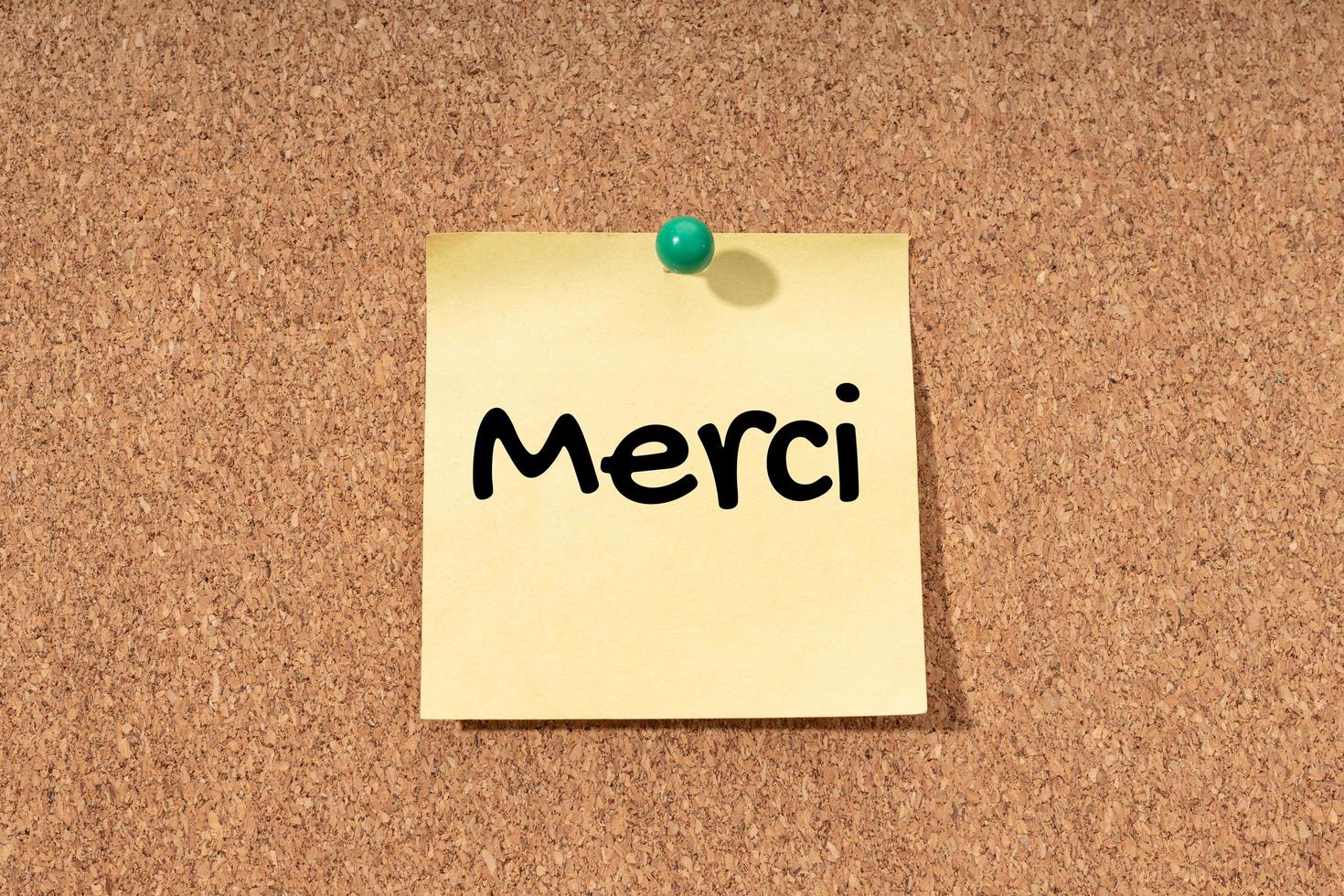 Merci - Thanks word in French language on yellow note on cork board photo