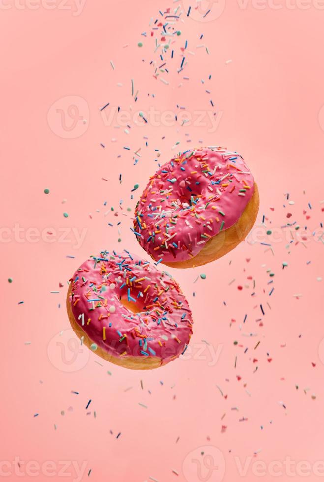 Dos donas levitando con chispitas de azúcar sobre un fondo de color rosa foto