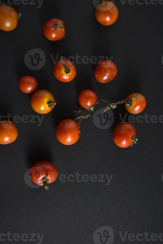 Tomates cherry planos yacen sobre fondo negro foto