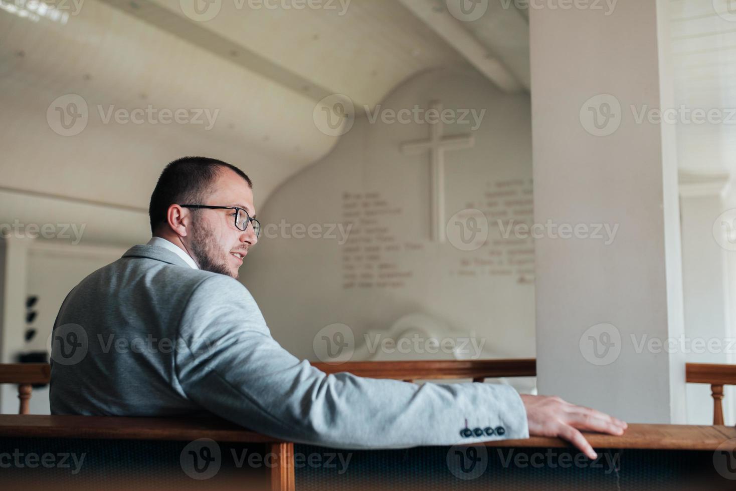 Wedding photo of emotions of a bearded groom with glasses in a gray jacket in the church building