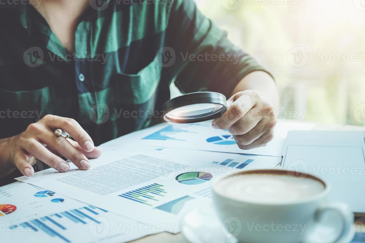 Business man using magnifying to review balance sheet annual with using laptop computer to calculating budget photo
